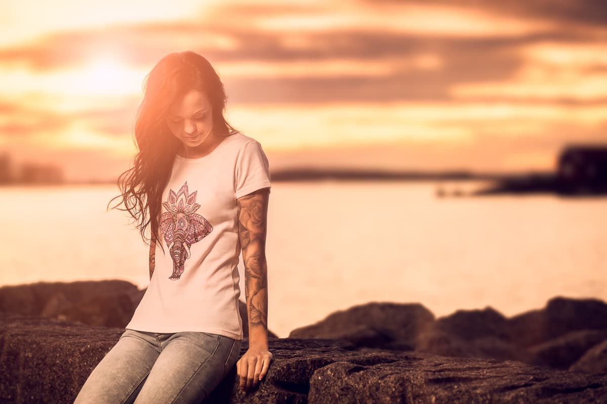 Kvinne i T-skjorte med elefanttrykk ved havet i solnedgang